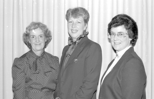 Black and white photo of Zonta Club Guelph executive members Joan Smith, Mary Skerritt and Elizabeth Honneger, at general club meeting. Taken on May 22, 1984. Joan Smith is wearing a polka dotted shirt, Mary Skerritt in the middle is wearing a pant suit and Elizabeth Honneger is wearing a pantsuit with glasses.