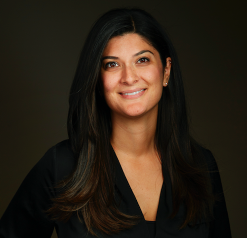 A professional head shot of Shakiba Shayani. She is smiling facing the camera wearing a black dress with a generic photography background behind her.
