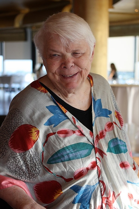 A photograph of a smiling Jean Little. Her hair is very short and light grey and she wears a colourful shawl over a black shirt.